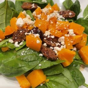 bed of spinach on plate topped with butternut squash, pecans and goat cheese