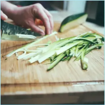 wood chopping board with hands chopping fresh zucchini into strips