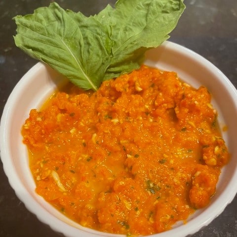 Roasted red pepper sauce in white bowl garnished with fresh basil leaves
