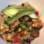 colorful bowl of quinoa studded with corn, tomatoes, fresh cilantro and black beans. Topped with avocado slides