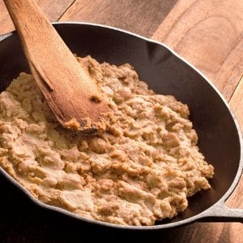 Low sodium refried beans in a cast iron skillet and wooden spoon