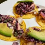 picture of 4 fish tacos topped with avocado and purple cabbage slaw