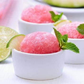 Frozen watermelon sorbet in a white dish garnished with fresh mint and lime wedges