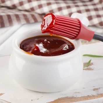 Picture of low sodium BBQ sauce on silicone brush out of a white crock