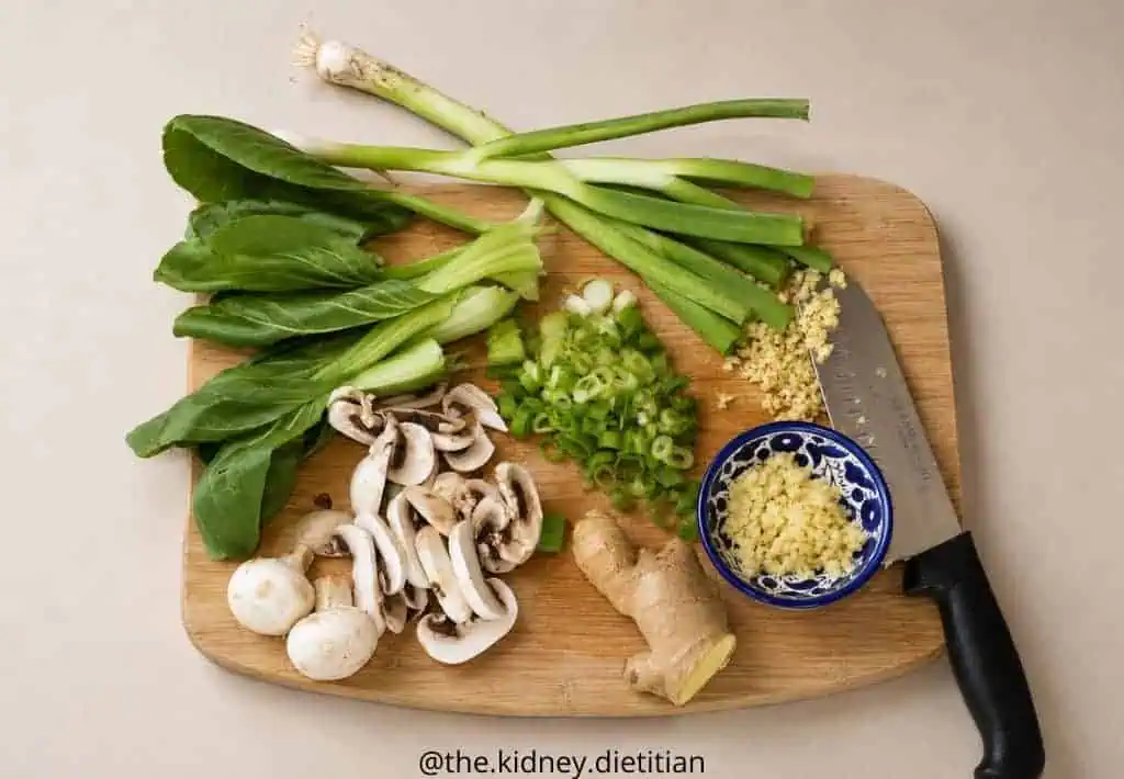 Cutting board with low sodium ramen ingredients on it - green onions, baby bok choy, mushrooms, ginger and garlic